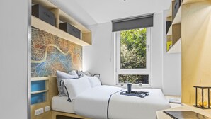 Un dormitorio pequeño con cama, estantes empotrados, un mapa en la pared y una ventana con vista a follaje.