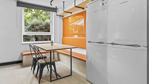 Una cocina moderna con un refrigerador blanco, una mesa de madera con sillas y una ventana con vista a árboles.