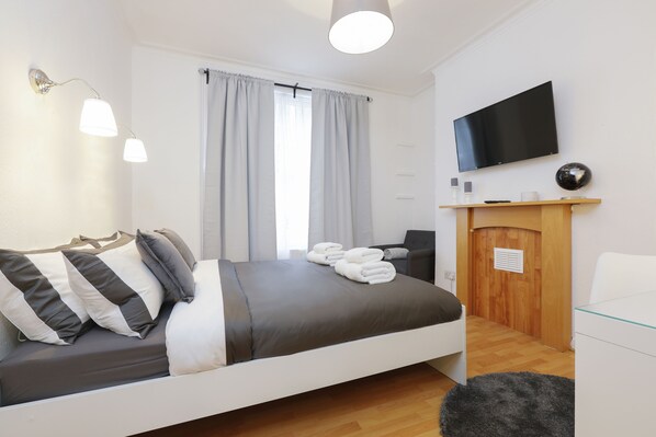 A modern hotel room with a bed, a sofa, a TV, and a wooden cabinet.