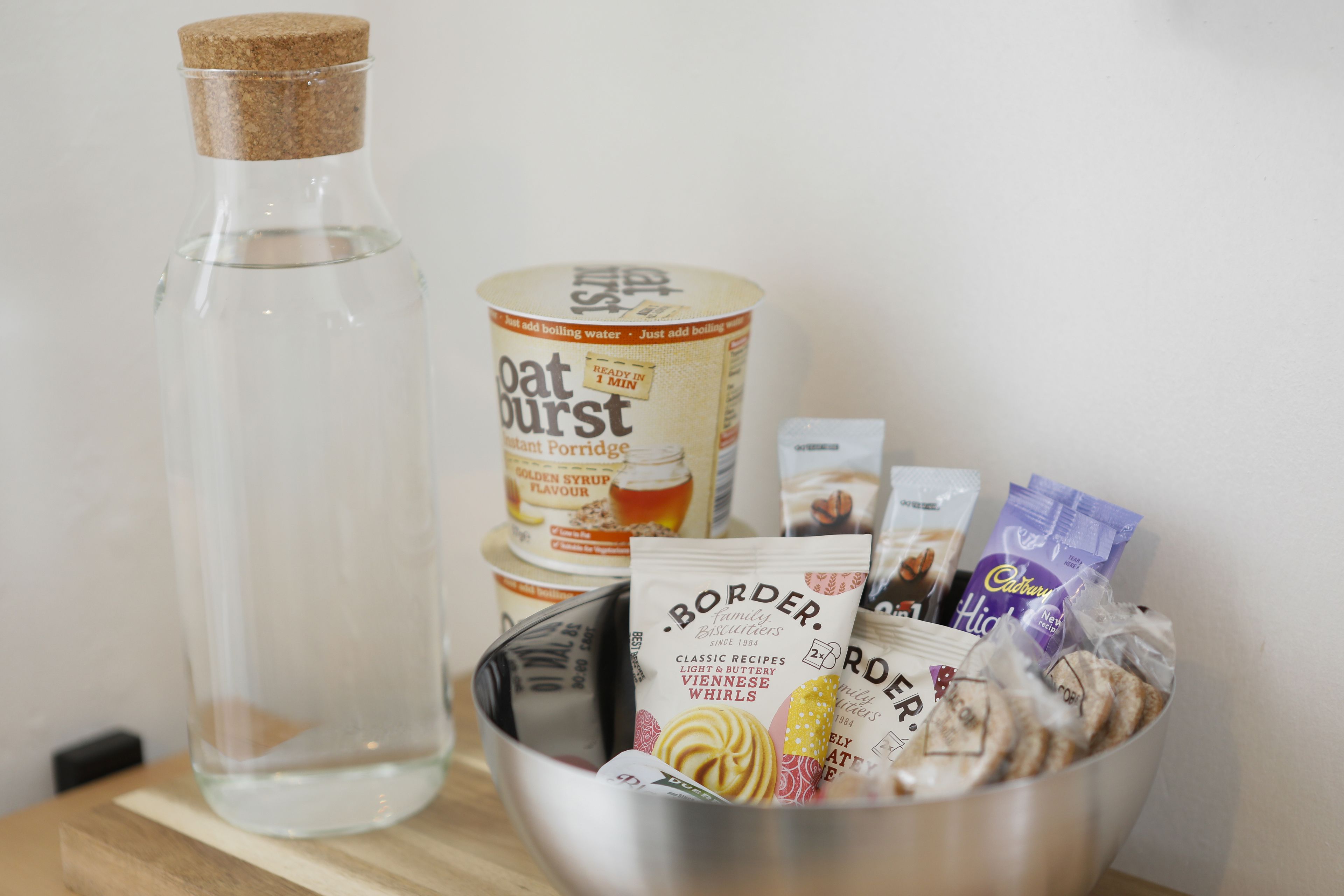 A clear glass bottle, a canister, and a metal bowl containing packaged food items.
