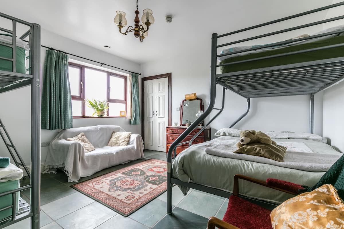 A dormitory room with bunk beds, a sofa, a dresser, and a window with curtains.