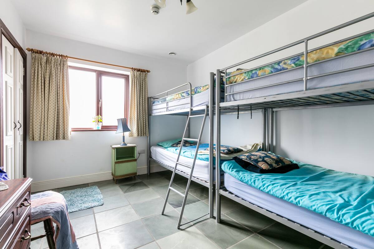 A dormitory room with bunk beds, a desk, a lamp, and a window with curtains.