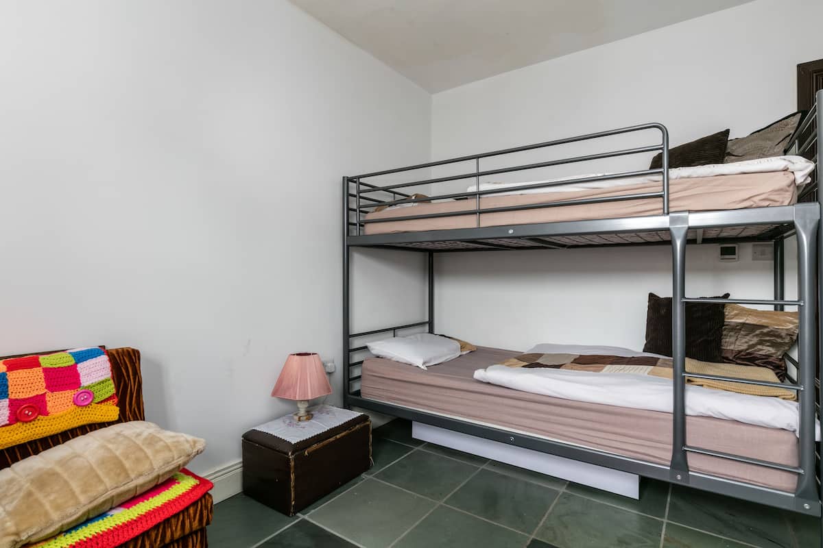A bunk bed room with a small table, a lamp, and a colorful blanket.