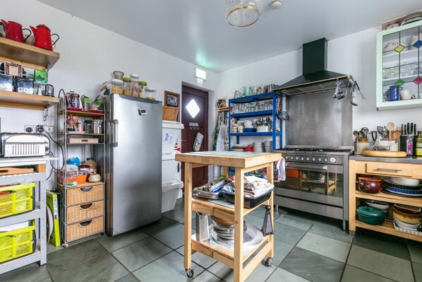 Una cocina con un refrigerador de acero inoxidable, una estufa a gas y varios utensilios de cocina en estantes.