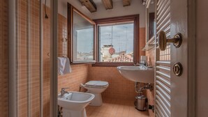 Ein Badezimmer mit Toilette, Bidet, Waschbecken und einem Fenster mit Blick auf Gebäude.