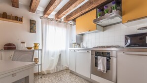 Eine Küche mit weißen Schränken, einem Edelstahlbackofen, einer Mikrowelle und einer Holzbalkendecke.