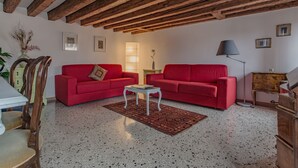 Ein Wohnzimmer mit zwei roten Sofas, einem kleinen weißen Tisch, einer Lampe und einem Holzkasten.