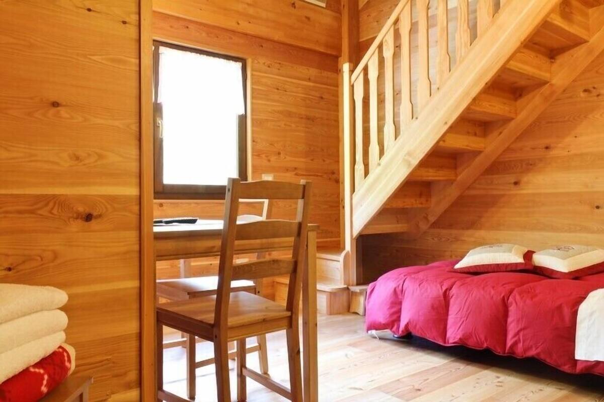 A wooden cabin room with a wooden chair, a bed with a red blanket, and a staircase.