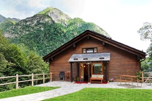 A wooden cabin with a stone pathway leading to the entrance, surrounded by lush greenery and mountains in the background. - Agriturismo Alagna (Alagna Valsesia)