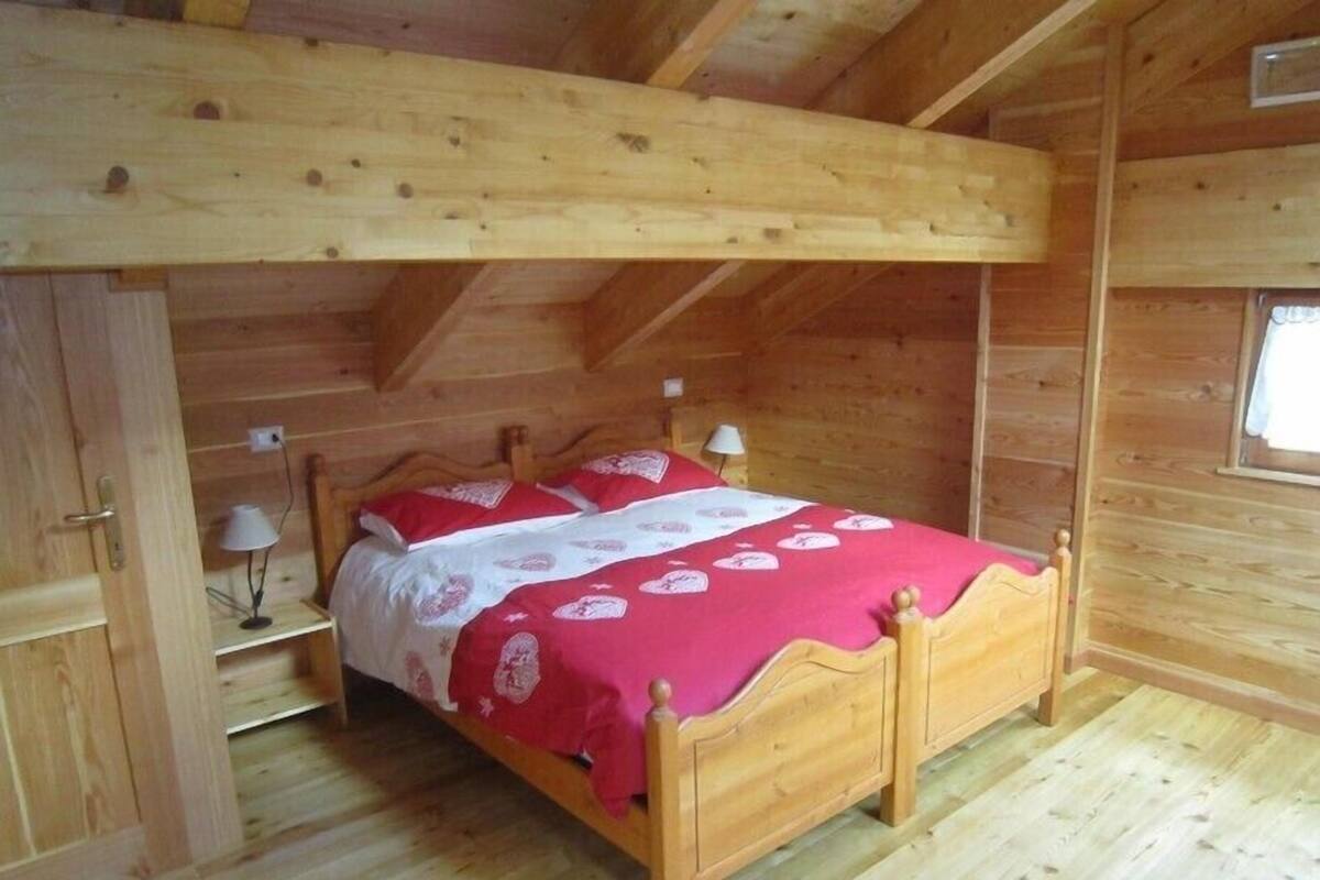 A wooden cabin bedroom with a bunk bed, a nightstand, a lamp, and a window.