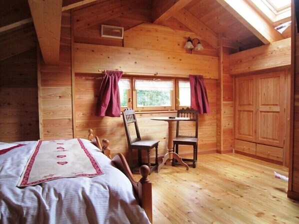 Une pièce chaleureuse, aménagée dans un chalet en bois, avec un lit, une table et des chaises, une fenêtre avec des rideaux et une armoire.