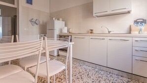 A modern kitchen with white cabinets, a granite countertop, and a sink. There are white chairs and a refrigerator. - Lido Venezia - Via Smirne 9 (Venice)