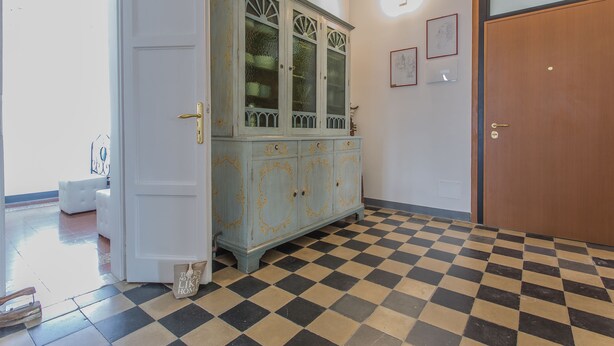 A room with a checkered floor, a white door, a wooden door, and a light blue cabinet with glass doors. - Lido Venezia - Via Smirne 9 (Venice)