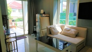 A modern living room with a glass coffee table, a sofa, and a chair. There is a sliding glass door leading to a balcony with a view of a house and greenery. - 3BRs 5 BathRms with private pool in BKK, 3 km to metro ,9 km to BKK airport (Bangkok)