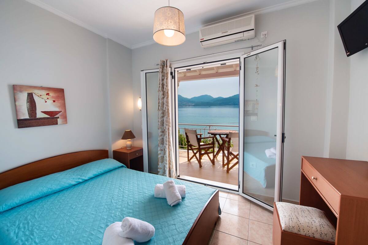 Habitación de hotel con cama, escritorio, silla, mesa y balcón con vista al mar.