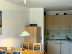 Uma cozinha compacta com armários de madeira, uma mesa de jantar com cadeiras e um lustre.