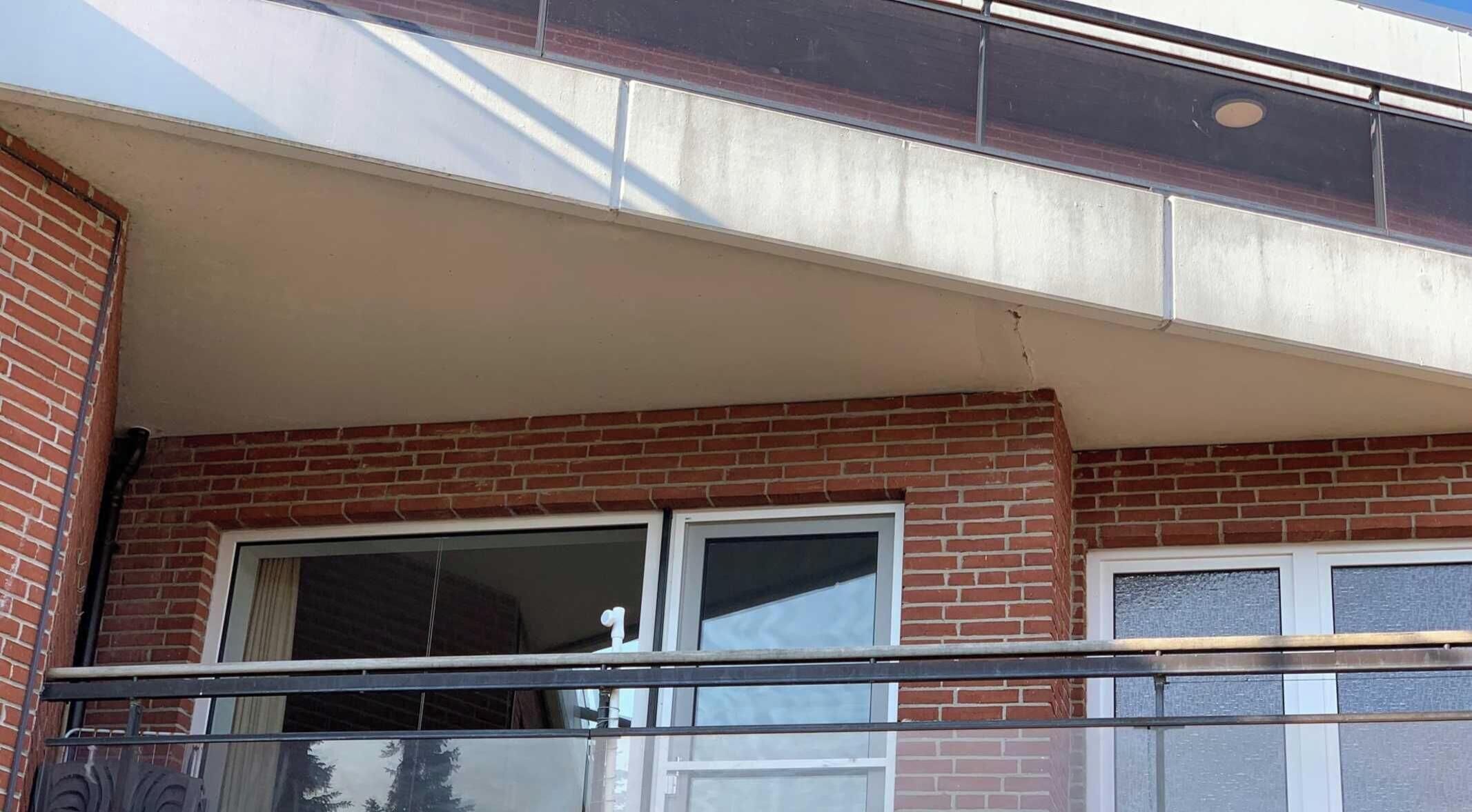 Un edificio con fachada de ladrillo, dos ventanas con marcos blancos y un balcón con barandilla de metal.