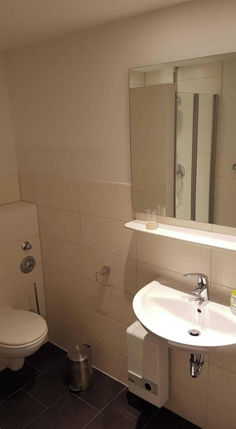 A bathroom with a toilet, sink, mirror, and shower.