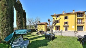 A yellow building with a balcony, a grassy yard, and a striped chair with a canopy. - Apartment Rosa Cinderella With Pool (Lazise)