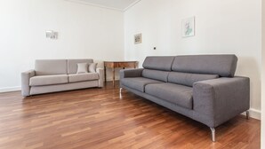 A modern living room with a grey sofa, a smaller grey armchair, and a wooden side table. - Venezia - San Pantalon 3700 (Venice)