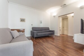 A modern living room with a grey sofa, a wooden floor, and a flat-screen TV on a white stand. - Venezia - San Pantalon 3700 (Venice)