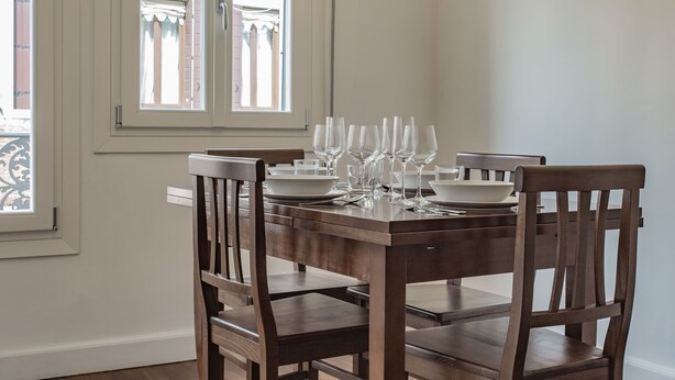 A dining table set with multiple wine glasses and plates, positioned near a window with a view of a balcony. - Venezia - San Pantalon 3700 (Venice)