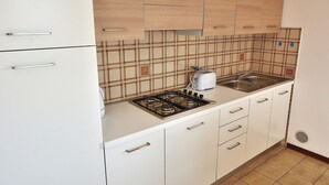 A kitchen with white cabinets, a gas stove, a sink, and a tiled backsplash. - Apartment Rosa Portland With Pool (Lazise)
