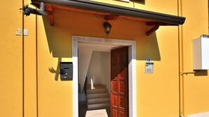 A yellow building with a wooden door, a mailbox, and a number sign indicating the entrance. - Apartment Rosa Portland With Pool (Lazise)