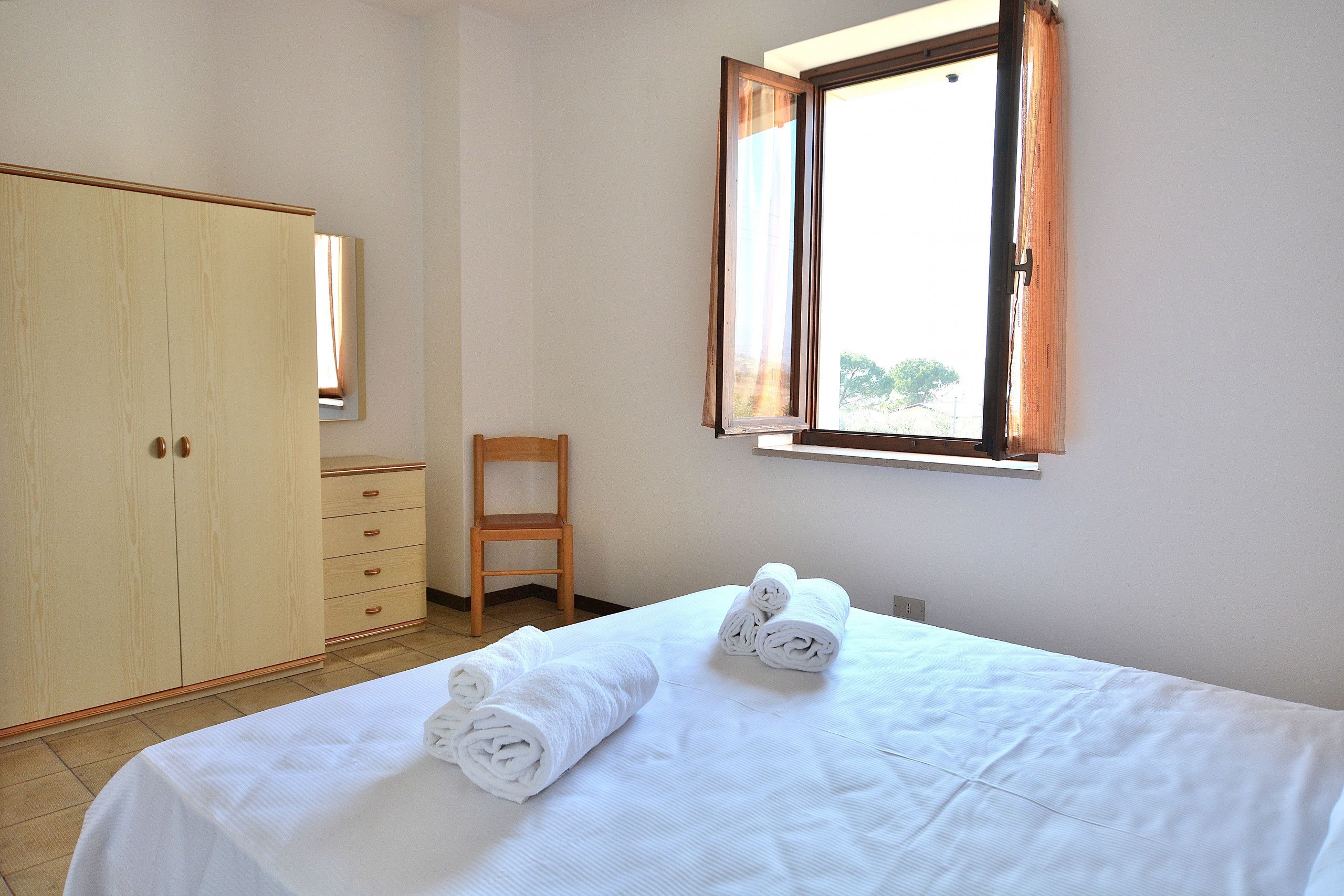 A bedroom with a bed, a wardrobe, a chair, and a window with curtains.