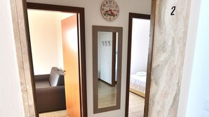A hallway with a tiled floor, a door with a number '2' sign, a clock, and a bed in the background. - Apartment Rosa Portland With Pool (Lazise)