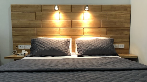 Un lit recouvert d’une courtepointe grise, deux tables de chevet avec des lampes, et une tête de lit en bois agrémentée de deux lampes fixées au mur.