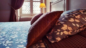 A bed with a floral bedspread and patterned pillows, a window with curtains, and a bedside lamp. - Château de Belle-Vue (Sainte-Cecile)