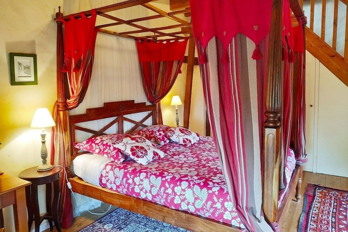 A four-poster bed with red curtains, a wooden headboard, and a patterned bedspread.