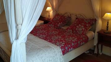 Een hemelbed met witte gordijnen, een rode bloemenovertrek en een witte quilt.