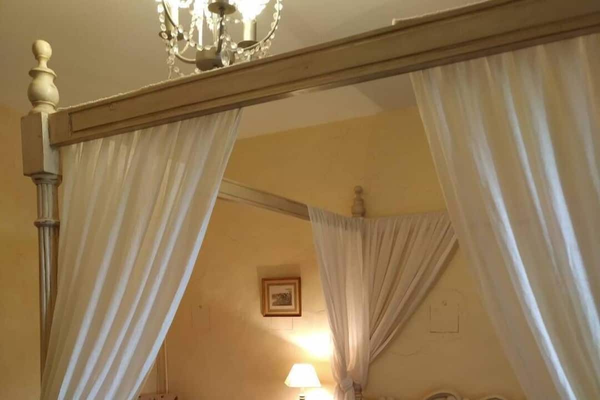 A four-poster bed with a canopy, a bedside table with a lamp, and a floral-patterned bedspread.