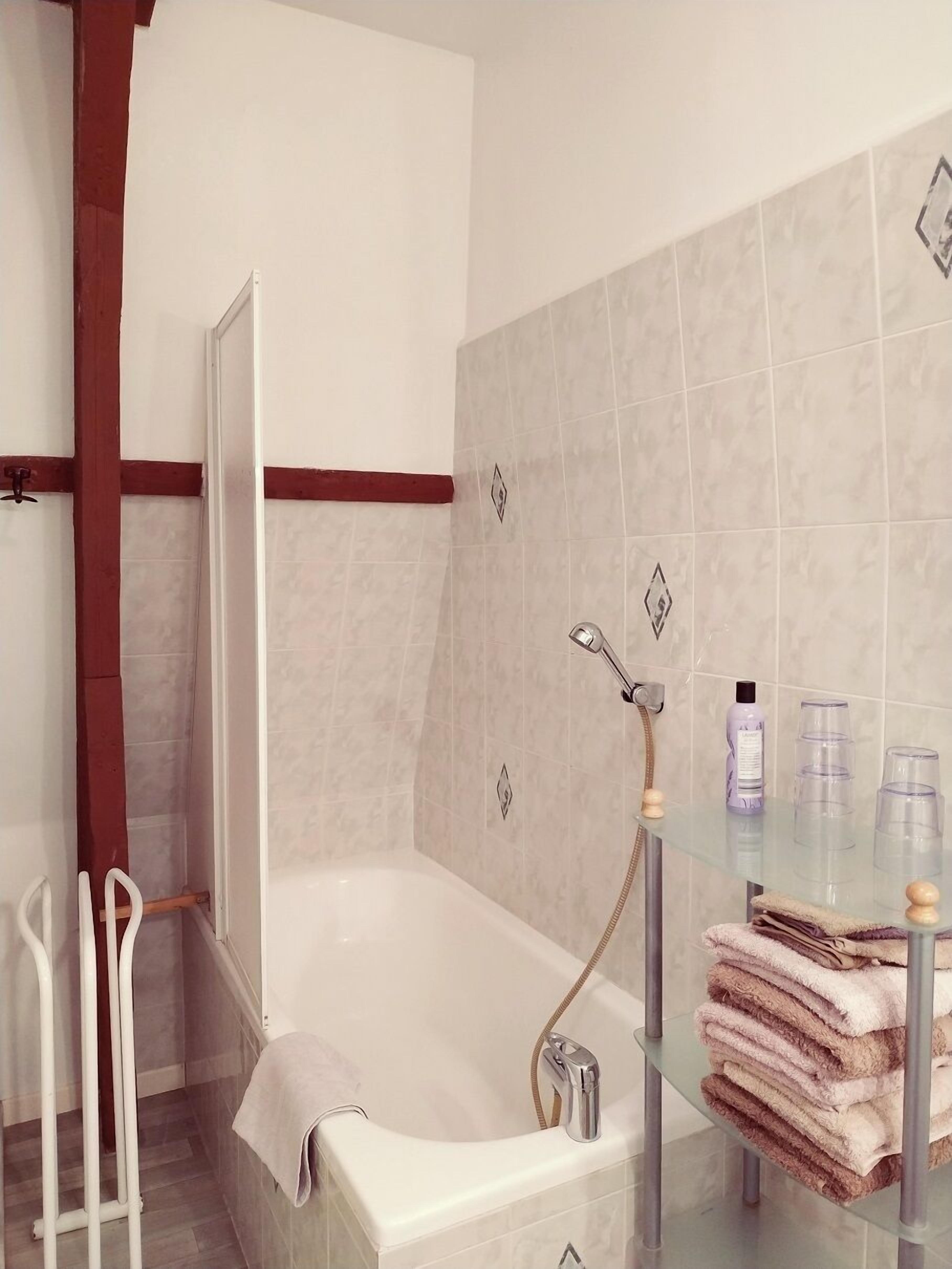 Une salle de bain moderne avec une baignoire, une étagère en verre où sont rangés les articles de toilette et un espace douche.