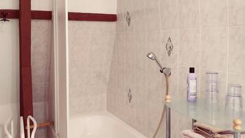 Une salle de bain moderne avec une baignoire, une étagère en verre où sont rangés les articles de toilette et un espace douche.