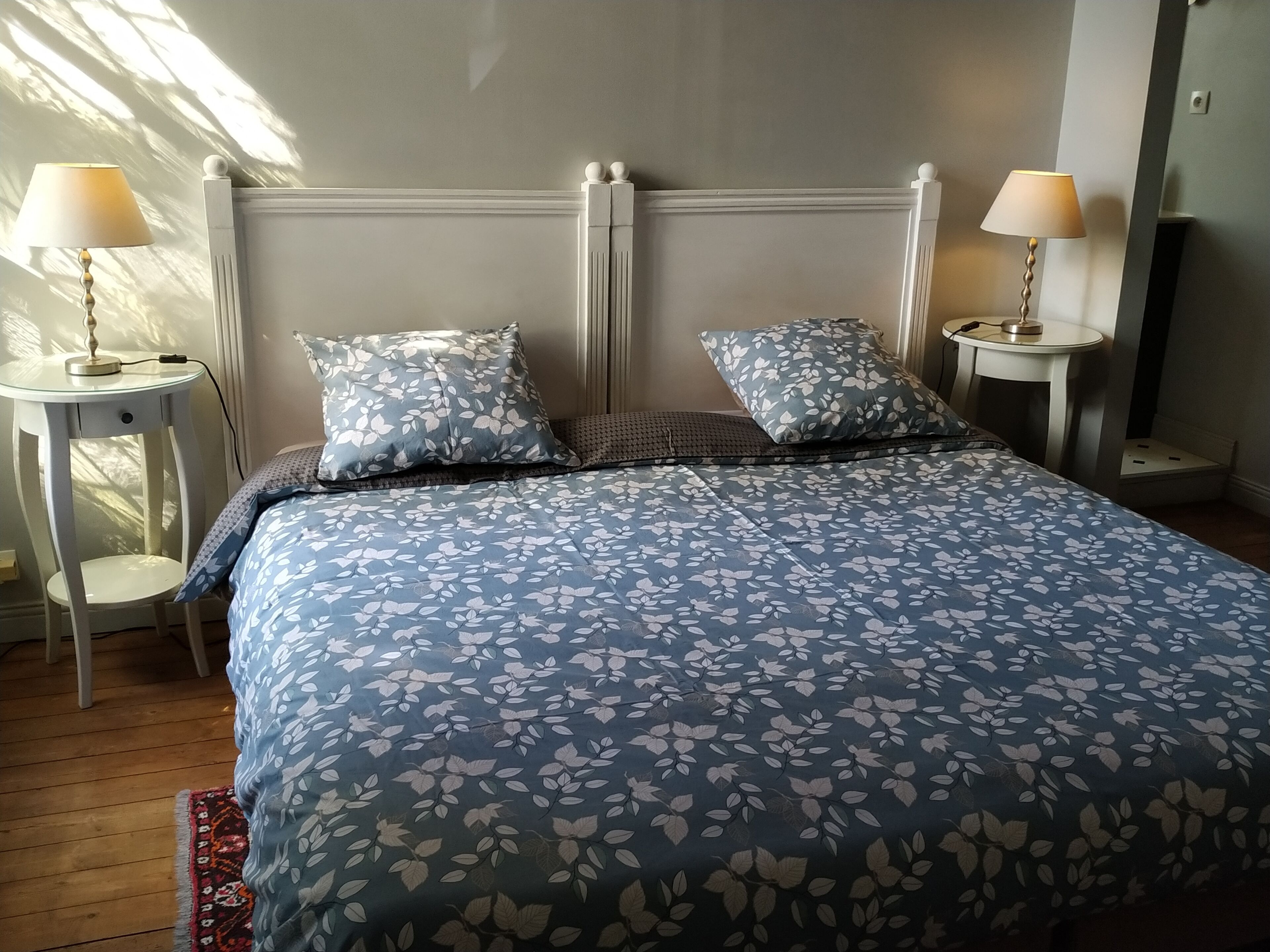 A neatly made bed with a floral-patterned bedspread, two matching pillows, and two bedside tables with lamps.