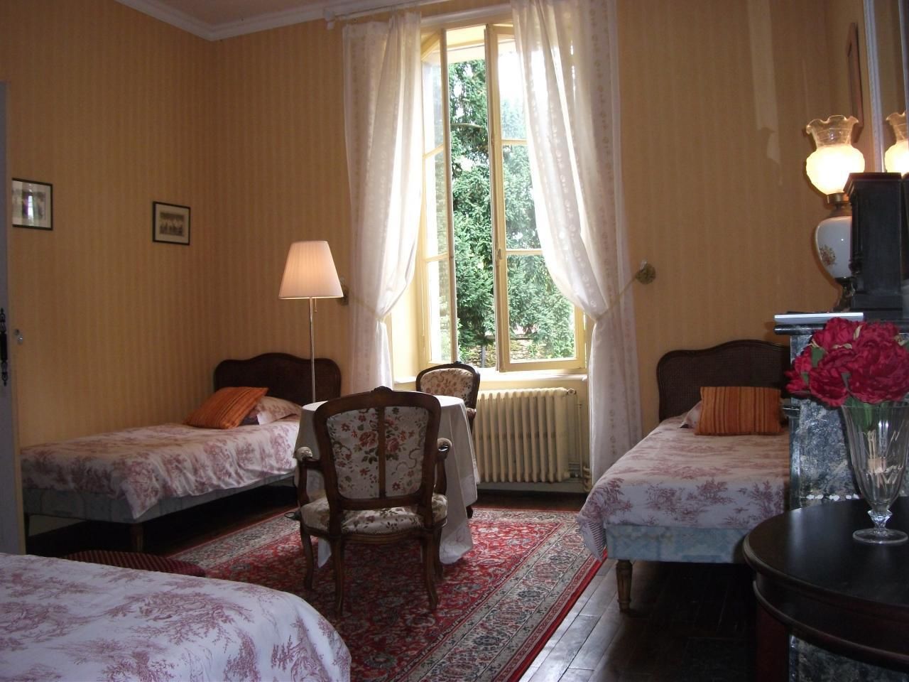 A hotel room with two single beds, a wooden chair, a table, and a radiator.