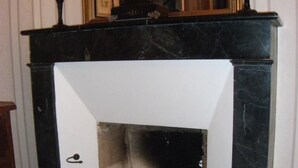 A fireplace with a clock above it, a mirror on the wall, and a door in the background. - Château de Belle-Vue (Sainte-Cecile)