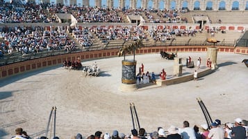 Uma arena de touradas com espectadores, um pilar central e um touro.