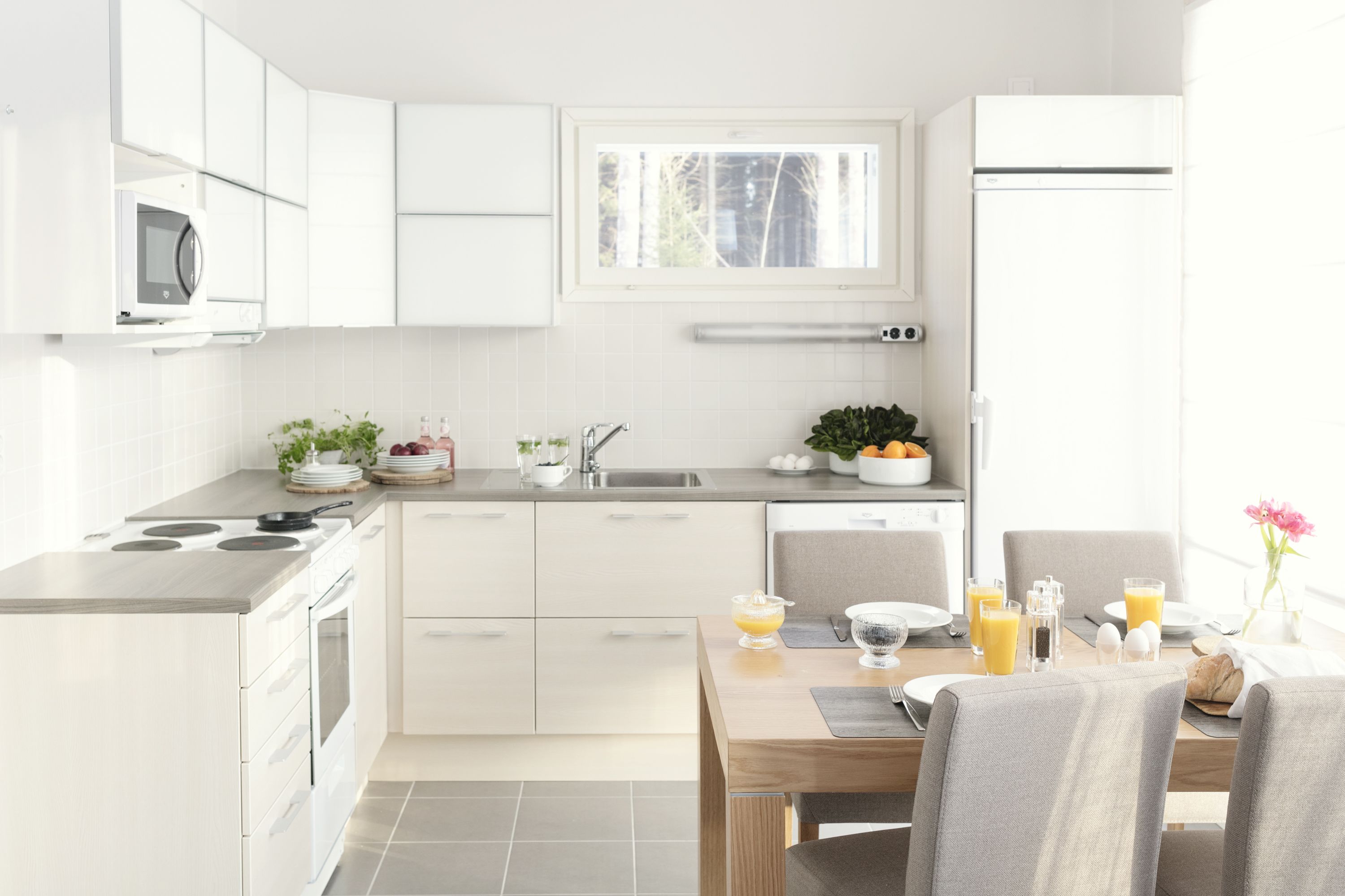 A modern kitchen with white cabinets, a built-in microwave, and a dining area with a table set for breakfast.