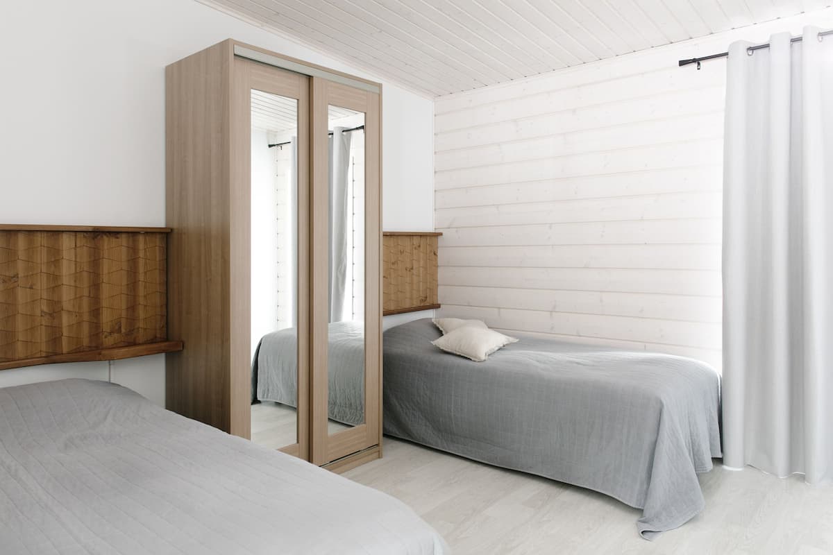 A bedroom with two beds, a wooden wardrobe, and a large mirror.