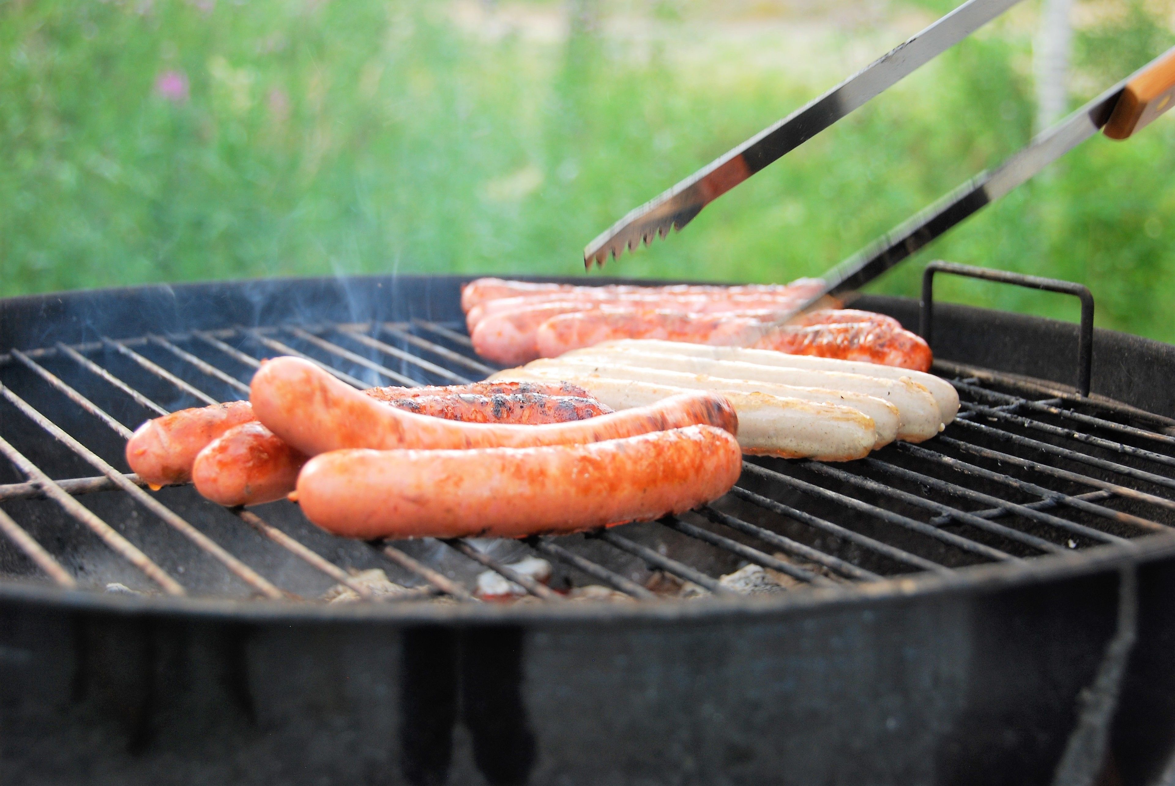 A grill with sausages being cooked outdoors.