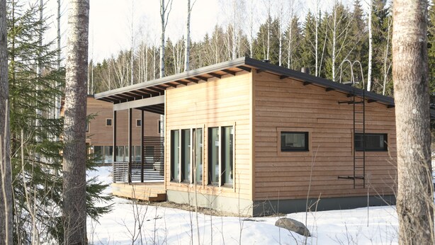 A modern log cabin with a deck and large windows, surrounded by a snowy forest. - Wooddream (Taipalsaari)
