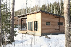 A modern log cabin with a deck and large windows, surrounded by a snowy forest. - Wooddream (Taipalsaari)