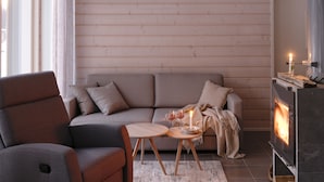 A modern living room with a sofa, a round wooden coffee table, a fireplace, and a large window. - Wooddream (Taipalsaari)