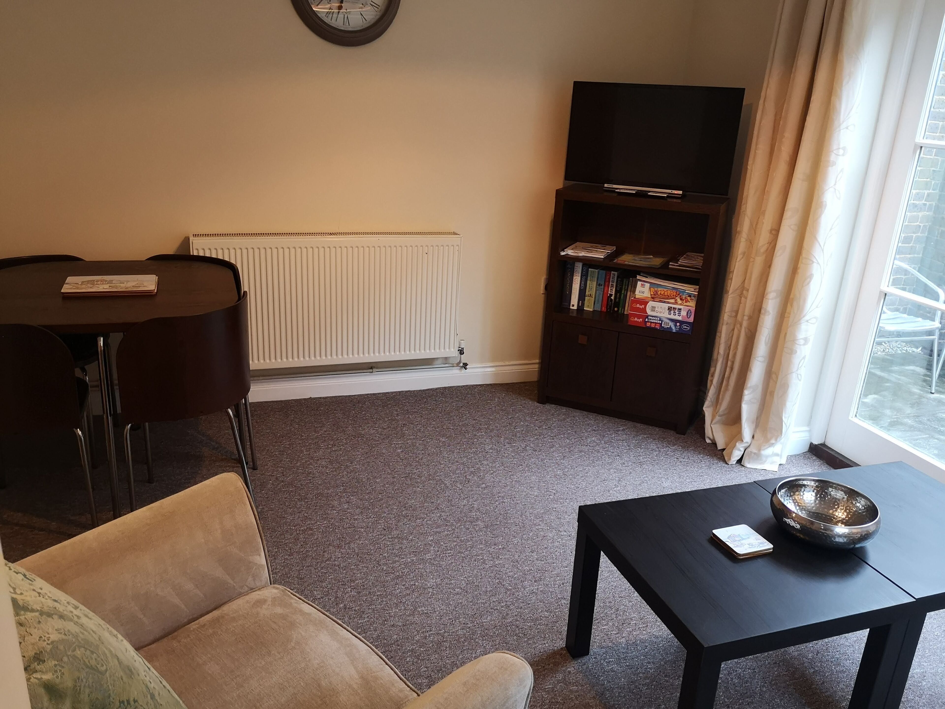A living room with a round table, a sofa, a bookshelf, and a window with curtains.