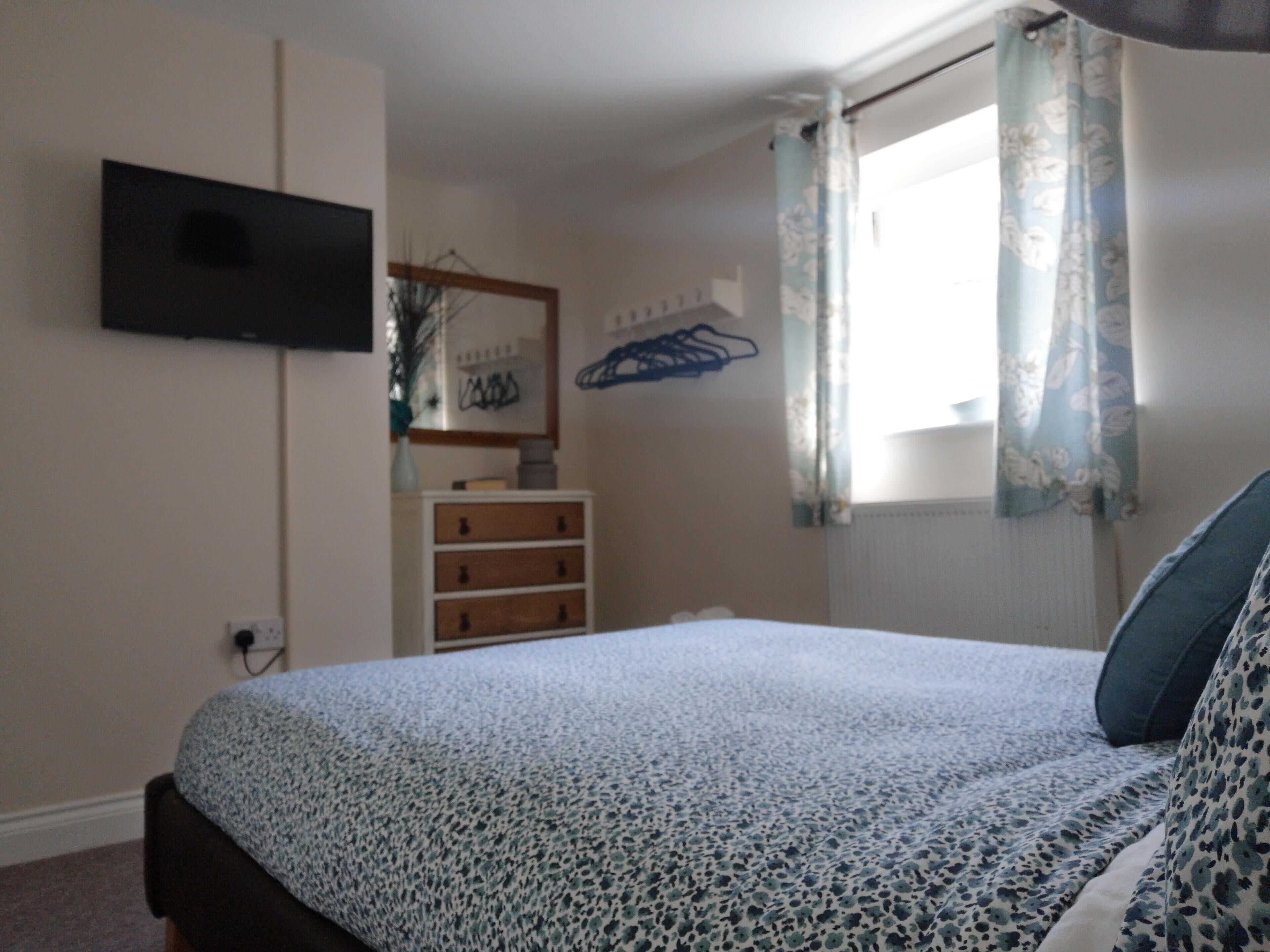 A bedroom with a bed, a dresser, a television mounted on the wall, and a window with curtains.