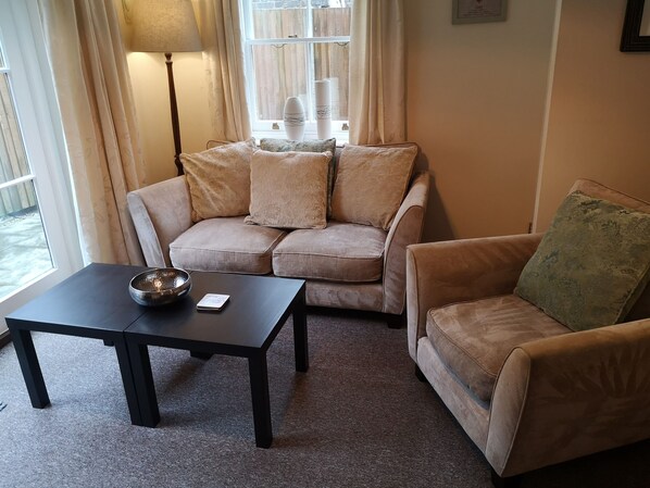 A living room with a beige sofa, a matching armchair, a black coffee table, and a floor lamp.